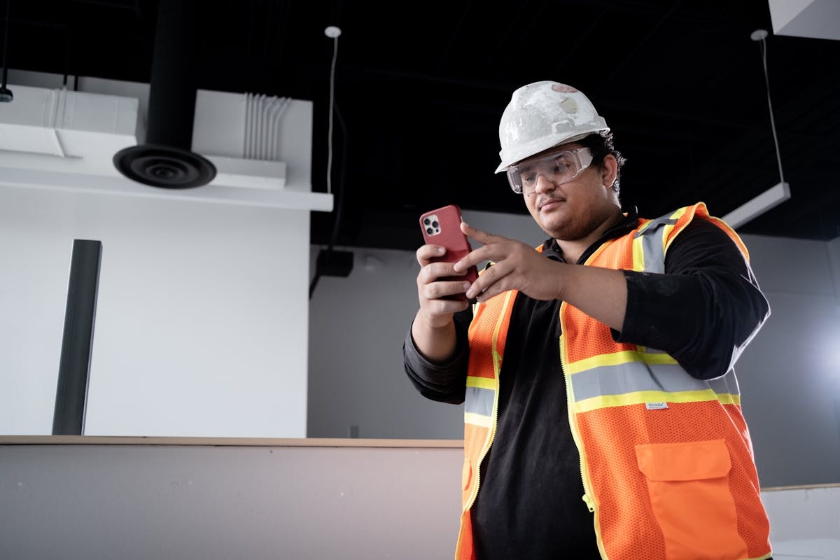 Construction worker in safety vest documents interior progress using mobile app on jobsite.