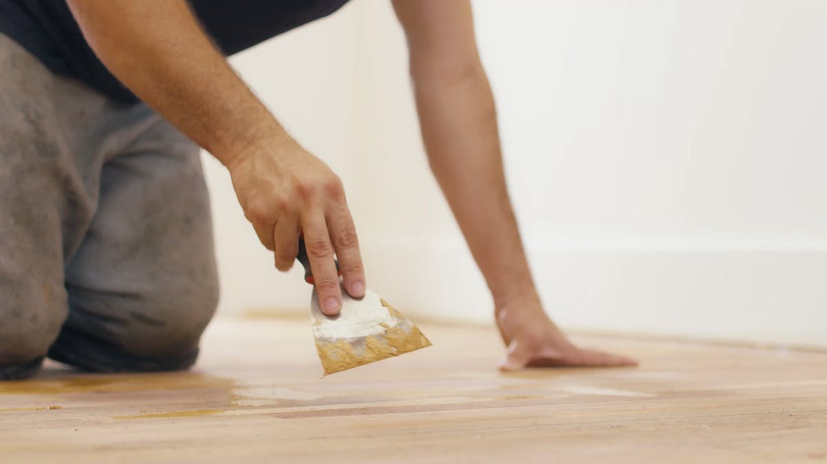 Contractor applying adhesive to a subfloor with a hand trowel during a flooring installation